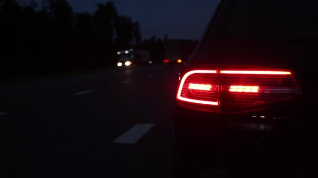 Red tail light of a passenger car parked on the side of the road in the evening. Vehicles with headlights are driving along the motorway. Roadside vehicle designation concept. Copy space for text