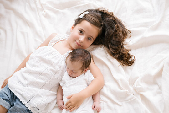 Smiling girl lying with newborn on bed
