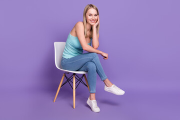 Full size photo of cool blond millennial lady sit wear teal top jeans sneakers isolated on violet color background