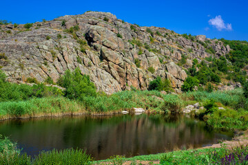 natural landscape mountain lake among the stone cliffs of the canyon overgrown with reeds and trees on a sunny summer day, nobody.