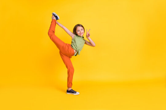 Full length body size photo little girl showing v-sign doing gymnastics isolated vivid yellow color background