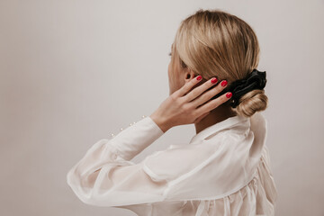Elegant young blonde-haired lady in white silk blouse and black scrunchie, adjusting trendy...