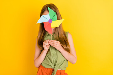 Obraz na płótnie Canvas Photo portrait schoolgirl wearing green shirt smiling hiding face with windmill isolated vivid yellow color background