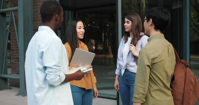 Smiling students standing at the street and discussing details of their project. Handsome multiracial man smiling to the camera at the background of his classmates