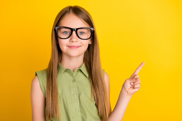 Photo of clever blond small girl point empty space wear spectacles khaki blouse isolated on yellow color background