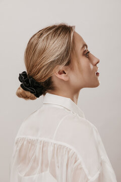 Profile portrait of gorgeous young blonde with classic hairstyle, pure skin and white blouse looking aside isolated over beige background