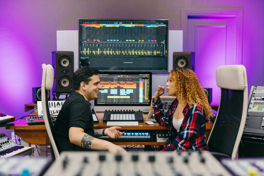 Sound engineer speaking with smiling black musician in music studio