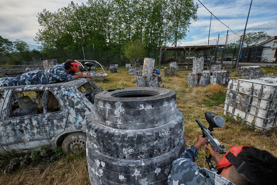 Anonymous men playing paintball near abandoned cars and barrels