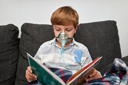Sick child in oxygen mask reading book at home