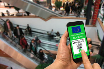 A man in a shopping mall holds a smartphone with the European Union digital green pass for Covid-19 in his hand. Safety concept for Coronavirus and the Green pass