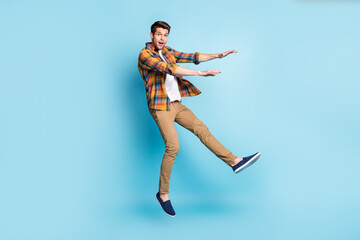 Photo of friendly cute young guy dressed plaid shirt smiling jumping high isolated blue color background