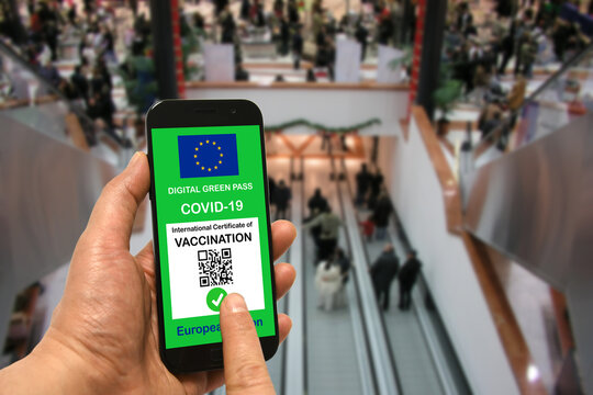 A man in a shopping mall holds a smartphone with the European Union digital green pass for Covid-19 in his hand. Safety concept for Coronavirus and the Green pass