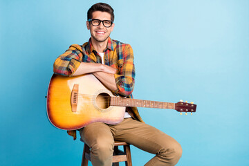 Photo of adorable cute guy dressed plaid shirt spectacles smiling siting chair holding guitar empty...