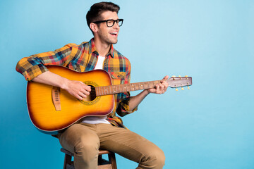 Photo of pretty adorable guy dressed plaid shirt spectacles smiling siting chair playing guitar...