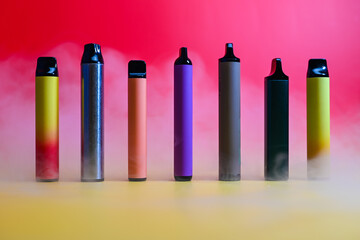multicolored vape electronic cigarettes on a red background in the smoke