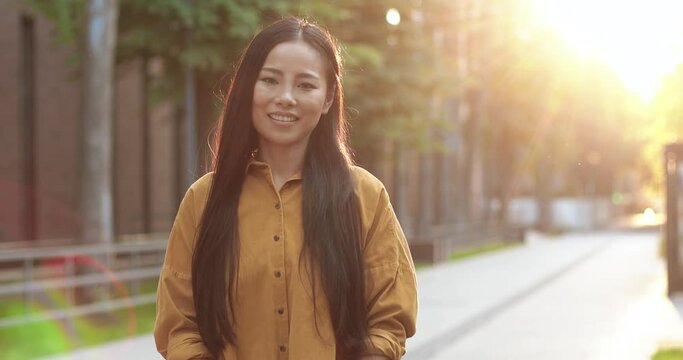 Portrait view of the asian student woman smiling toothy while spending break at the street at the sunset. Happy woman appearance concept