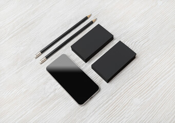 Smartphone, blank black business cards and pencils on light wooden background. Blank branding mockup.