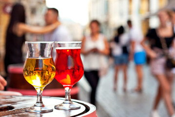 Glass of red and white wine close up. Alcoholic liqueur on a wooden barrel on a background of the city. Blurred people in the background.