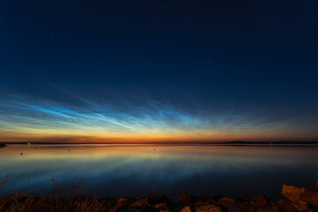 Night shining clouds (noctilucent clouds) over lake in Sweden, with kinnekulle in the background