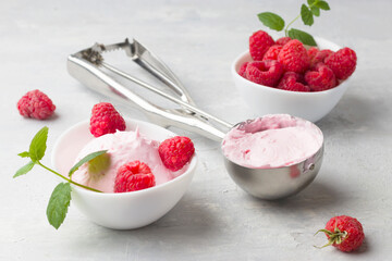 Fresh raspberries with mint and homemade ice cream in a white cup on a light background. Stainless steel spoon for ice cream balls. Delicious and romantic dessert.