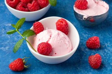 Fresh raspberries with mint and homemade ice cream in a white cup on a blue background. Stainless steel spoon for ice cream balls. Delicious and romantic dessert