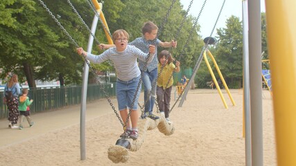 A group of teenagers ride a swing in a city park. They swing, hold chain with their hands. Swing...