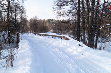 Fototapeta na wymiar Winter road over a wooden bridge in the forest