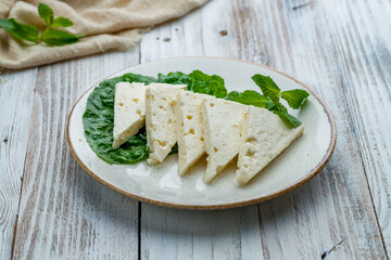 Suluguni cheese sliced on a plate on white wooden table