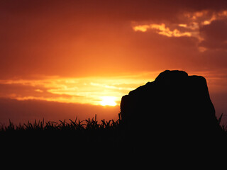 warm sunset over the silhouette of a rock and a grassy horizon