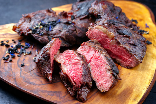 Traditional barbecue wagyu spider beef steak with black salt and spices served as close-up on a rustic wooden board