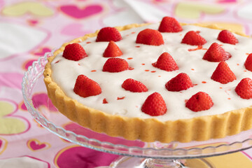 Strawberry tart with white cream on a romantic pink tablecloth decorated with hearts for Valentine's Day