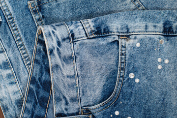 Close up on the front pocket stitching of a blue jeans with decorative ornaments glued to the...