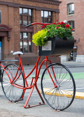 Fototapeta na wymiar Beautiful red painted bicycle with a bucket of colorful flowers on the street of the city.