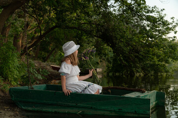 child in a boat. a little girl sits in a boat with a bouquet of flowers. a girl floats on the river.