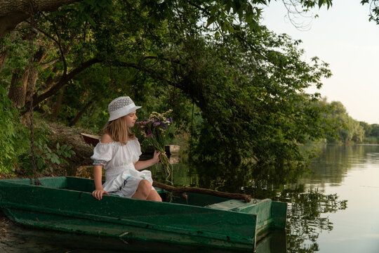 child in a boat. a little girl sits in a boat with a bouquet of flowers. a girl floats on the river.