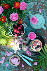 Fototapeta na wymiar Tartlets with jam and berries, teapot, flowers and fern branches on a turquoise background. View from above