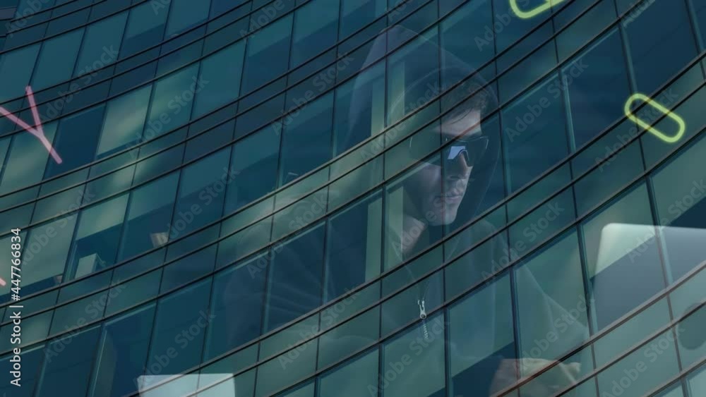 Poster multiple changing numbers and alphabets over male hacker using laptop against tall building