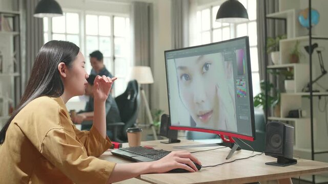 Tired Asian Female Digital Editor Works In Photo Editing Software On Her Personal Computer With Big Display In Office
