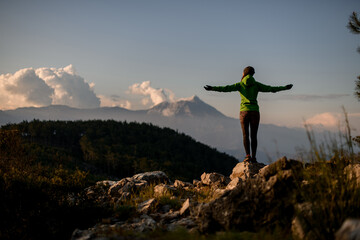 great rear view of woman with outstretched arms to sides against beautiful mountain landscape
