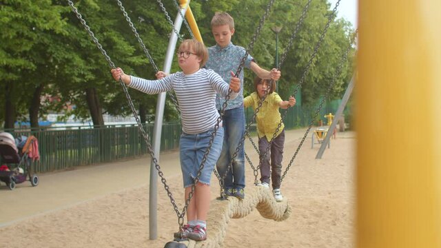 Children and teenagers swing the log on the chains with their feet. Group leisure activities at the city site. Exercise, body balance.