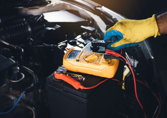 Technician clamping jumper cable for checking car battery voltage with digital multimeter