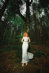 beautiful young red-haired bride in the forest. woman in long white dress outdoors on summer day. wedding day