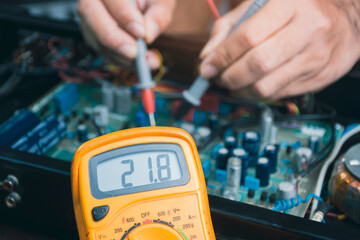 Electrician checking voltage of electronic circuit board with digital multimeter