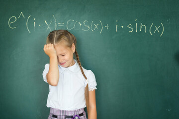 Child girl schoolgirl and compound formula on the chalkboard. Complex school program does not match the age of the child