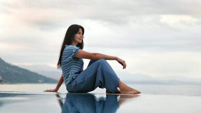 Casual brunette female relaxing at luxury spa resort endless sea swimming pool with mountain