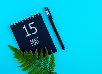 May 15th. Day  15of month, Calendar date. Black notepad sheet, pen, fern twig, on a blue background. Spring month, day of the year concept