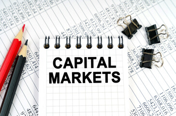 On the table are reports, pencils and a notebook with the inscription - CAPITAL MARKETS