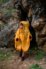 smiling woman tourist trekking poles wearing yellow raincoat emerges from cave