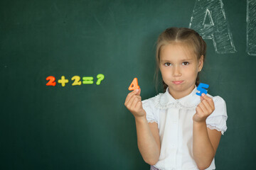 Pupil schoolgirl thinks over the blackboard. The child decides to examples in mathematics - 447773040