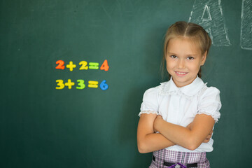 Pretty schoolgirl standing near blackboard and smiling